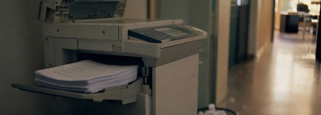 Una fotocopiadora de oficina con la tapa levantada y papeles olvidados en la bandeja de salida